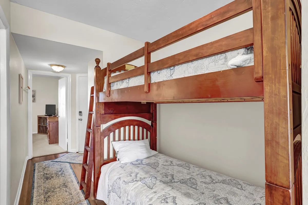 A cozy sleeping space featuring a bunk bed, floor rug, and a doorway that adds depth and a sense of privacy. The mood is playful yet quiet, making it suitable for children or extra guests seeking relaxation or a bedtime story.