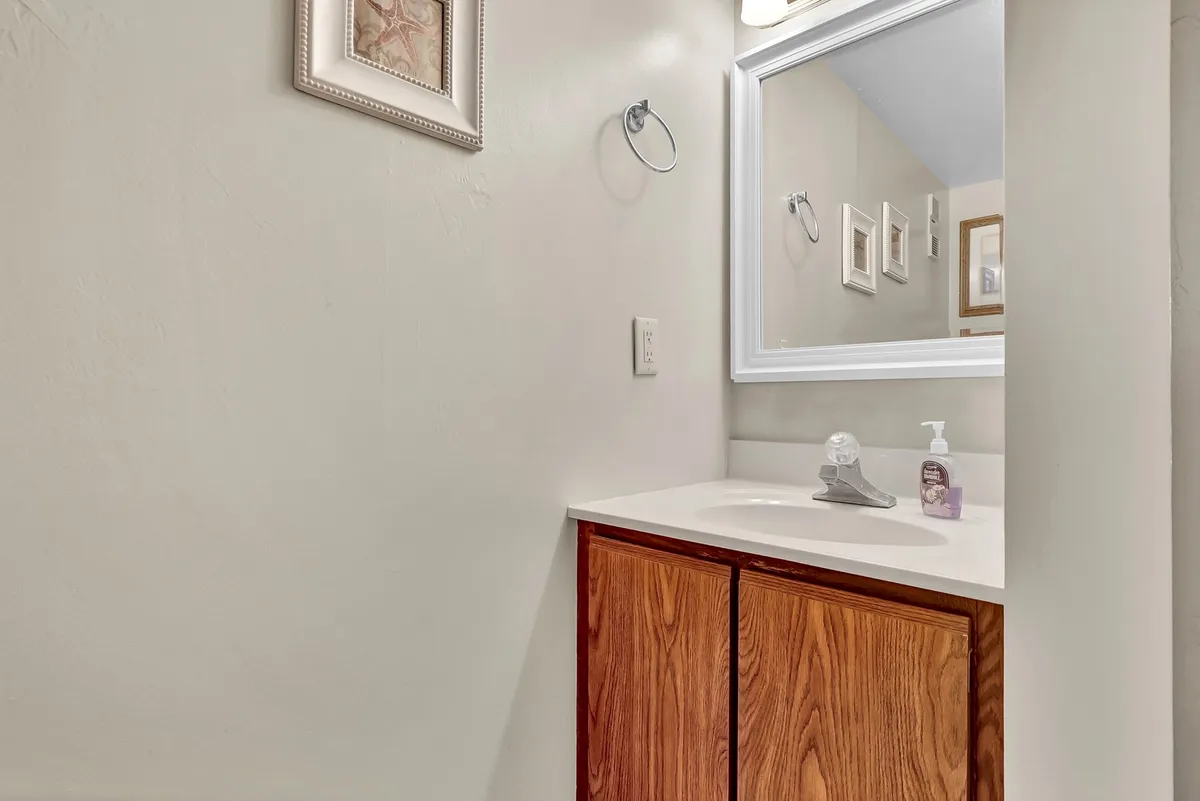 A half bath scene with a sink, mirror, wooden cabinets, and tasteful wall décor. The space feels calm and serene, ideal for personal grooming and providing convenience for guests and residents alike.