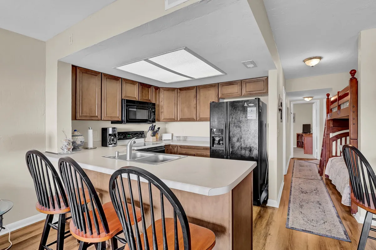 A warm, modern kitchen features a central island with bar stools, sleek appliances, and inviting cabinetry. The setup encourages casual bites at the breakfast bar and gatherings for meal preparation, capturing the home’s sociable spirit.