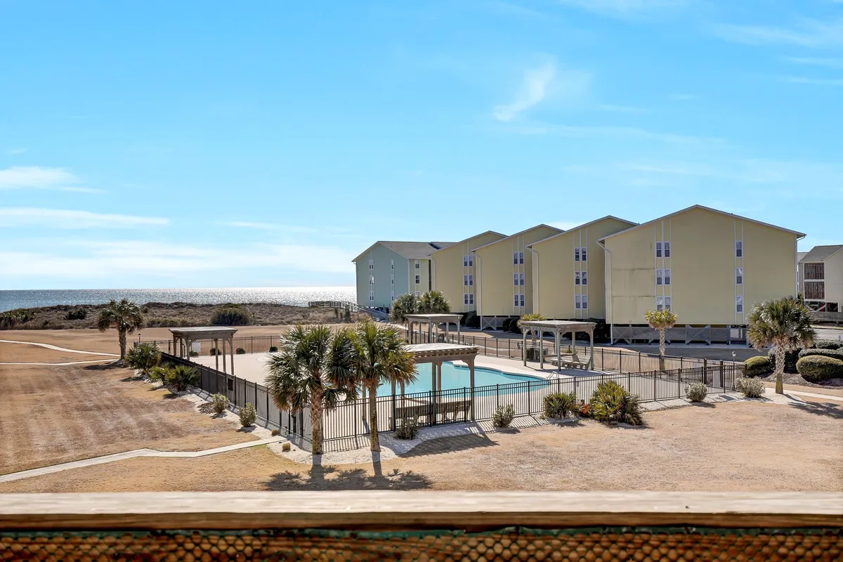 A tranquil pool surrounded by lush palm trees, with yellow beachfront buildings and the ocean just beyond. Families and guests relax poolside, while children play in the water. The scenery reflects a serene and accessible leisure area.
