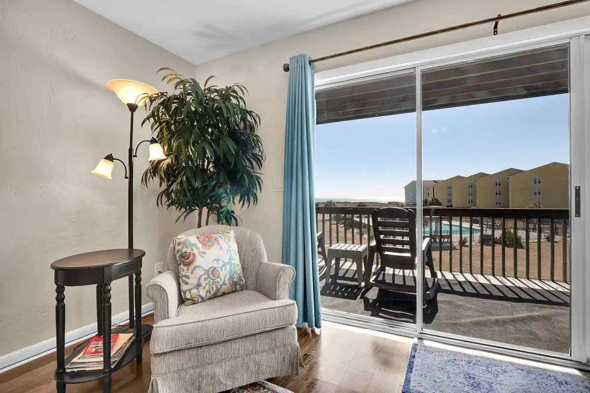 A cozy armchair and a potted plant sit next to sliding glass doors, which appear to open out to a balcony or patio. The doors suggest a connection between the indoor living space and the outdoors, inviting guests to enjoy sunrise views or step outside to begin their day of exploration.
