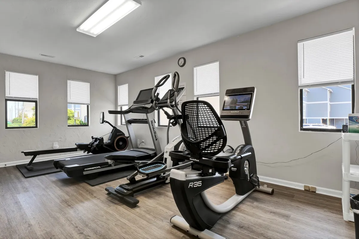 This image displays a well-equipped fitness room featuring exercise bikes and an elliptical machine, all positioned near large windows that let in plenty of light. The view hints at the possibilities of indoor activity within a bright, open atmosphere.