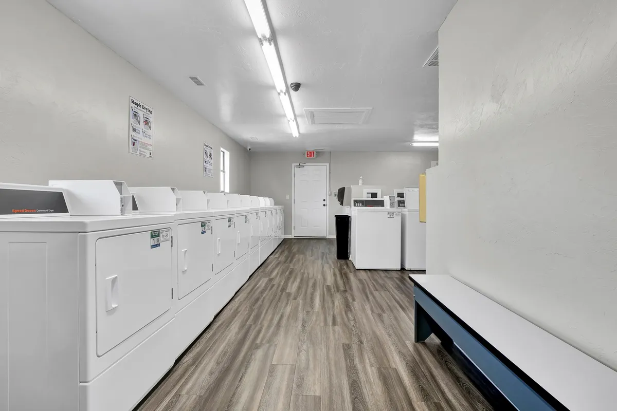 This image displays a row of white washing machines and dryers in a clean, organized onsite laundry facility, complete with a folding area.