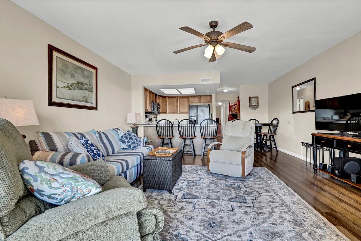 This image features a striped sofa, coffee table, recliner, a visible dining area, and a television—all arranged to foster comfort and togetherness. The décor is relaxed and inviting, echoing coastal and shabby chic influences.