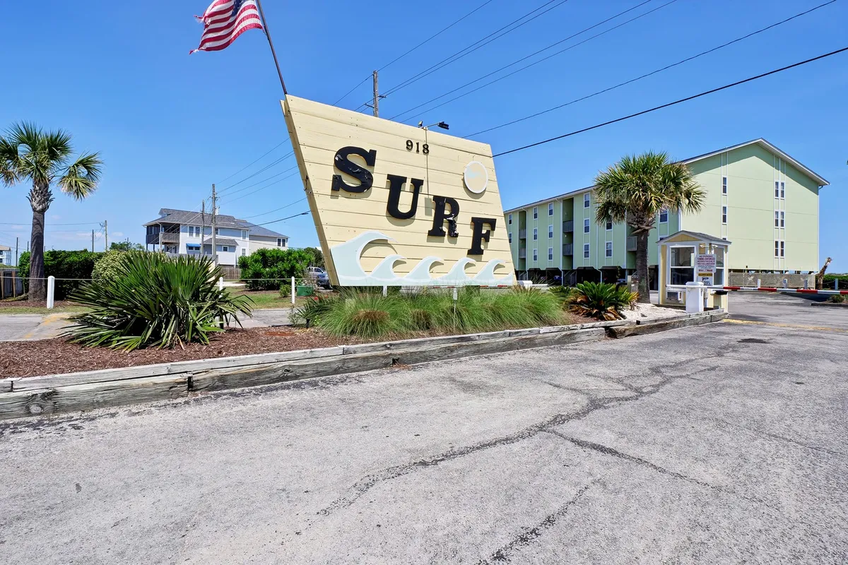 A cheerful exterior scene featuring a large 'SURF' sign, swaying palm trees, a vibrant yellow building, and an American flag—capturing the lively, welcoming spirit of Surf City’s community.