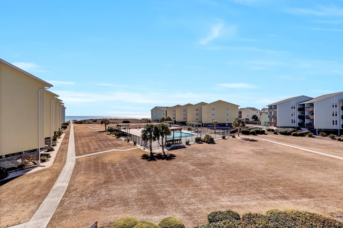 A sunlit outdoor swimming pool surrounded by well-maintained landscaping and community buildings. Lounge chairs border the water, providing ample space for sunbathing. The scene suggests an inviting and lively atmosphere ideal for both leisure and social gatherings.