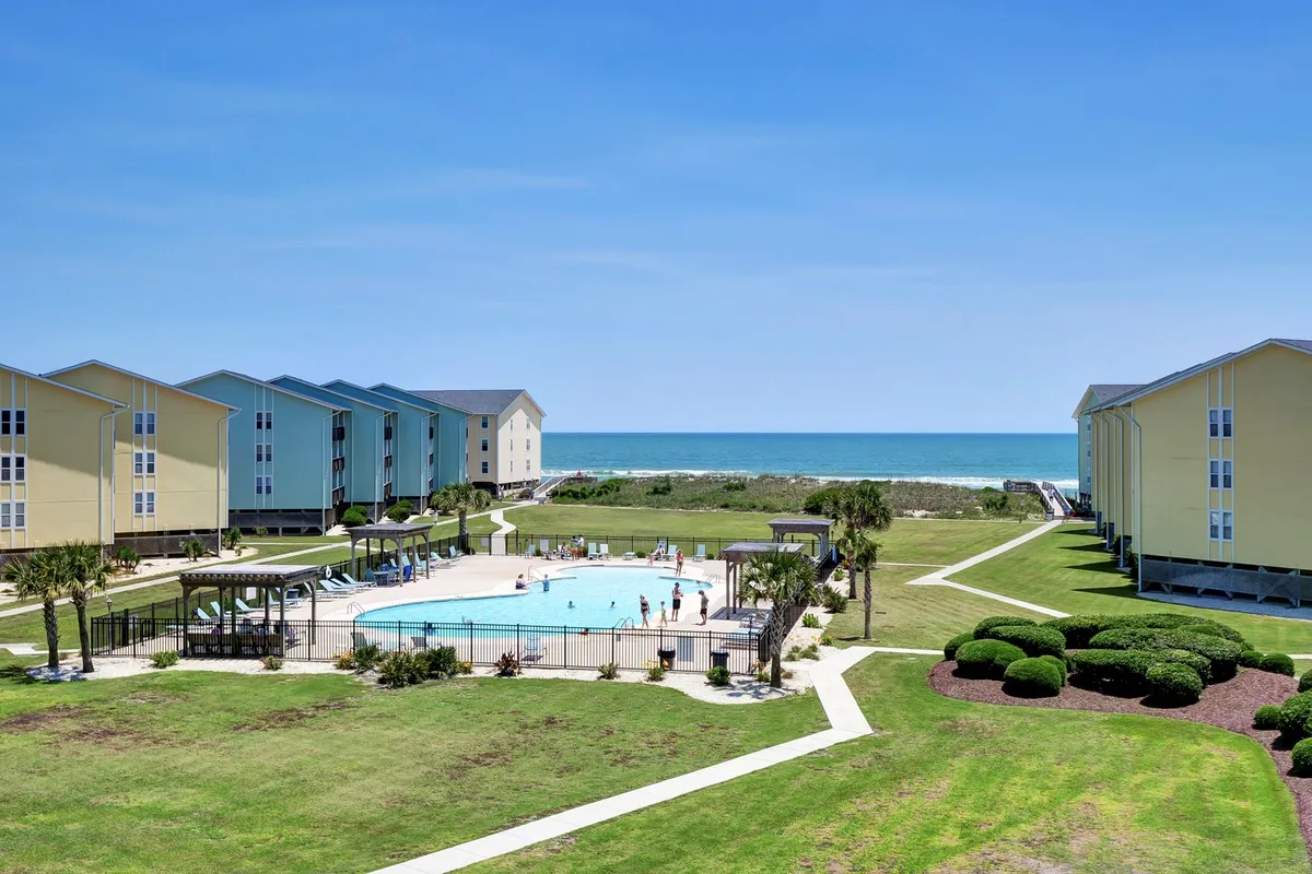 A scenic exterior shot showcasing a sparkling swimming pool, lush landscaped gardens, ocean views in the background, and residential buildings—blending relaxation with coastal scenery.