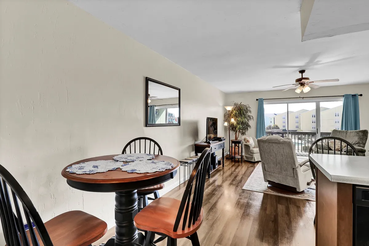 A round dining table sits near a large sunlit window, paired with a comfortable armchair, creating a welcoming spot for casual dining or morning coffee. The inviting setting suggests intimate meals or relaxed gatherings, echoing the social aspect of coastal dining.